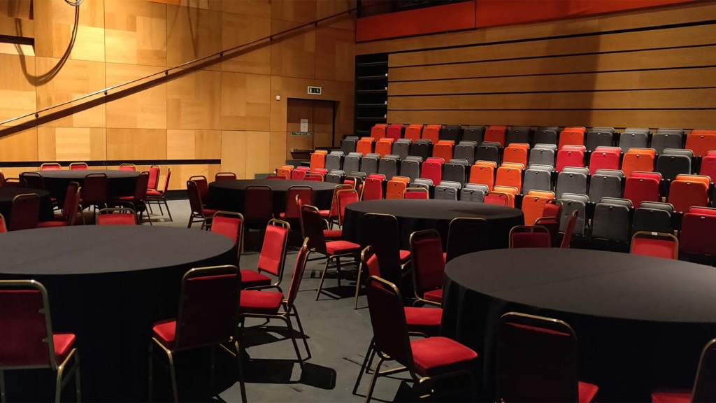 Several circular tables and chairs alongside a row of auditorium foldable seats.