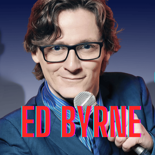 A close up image of comedian Ed Byrne wearing a formal blue suit and modern black glasses with thick frames.