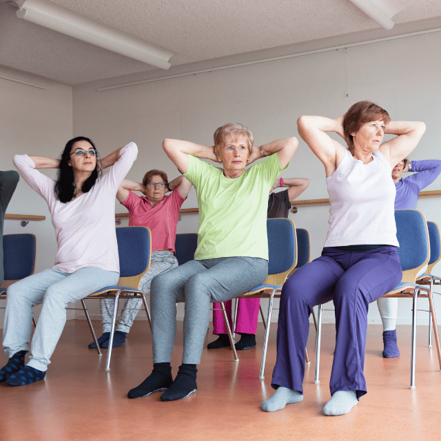 A group of old people doing exercises whilst sitting down on chairs.