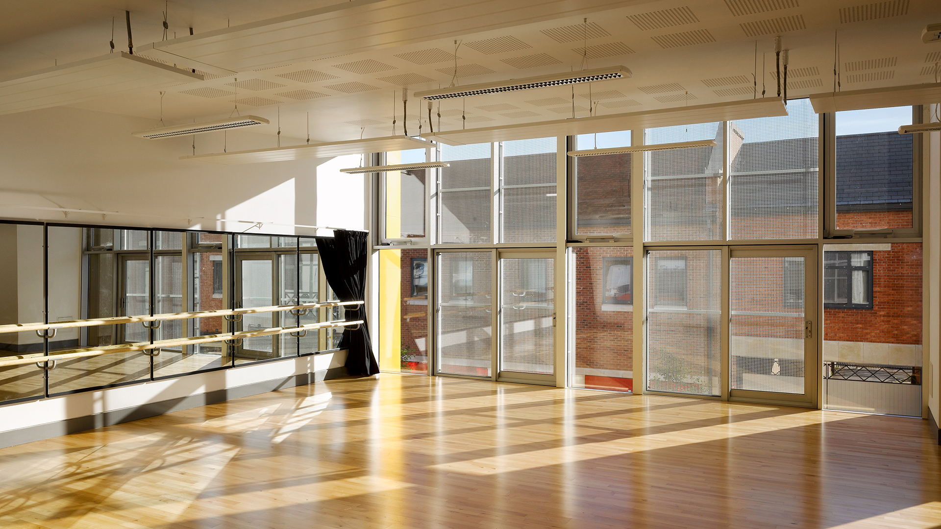 A studio space with laminate floors and a mirrored wall with a barre.