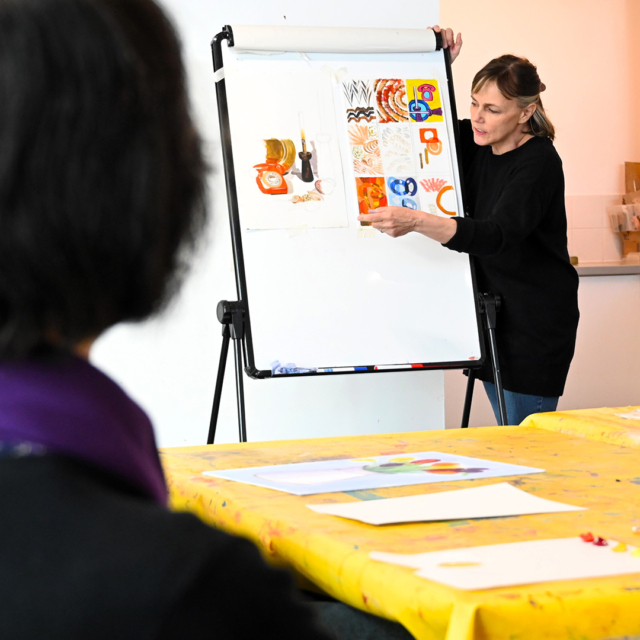 Someone holding different art prints on a whiteboard.