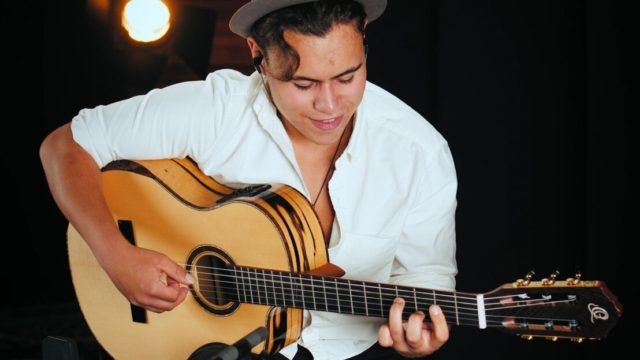 Billy Watman plays his guitar whilst smiling